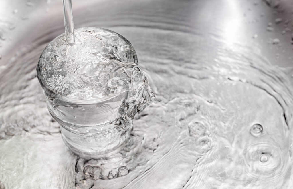 Pouring Water From Tap To Glass On Stainless Steel Stand At Kitchen Tone Filtered - Entsalzungsanlage Vs. Enthärtungsanlage: Ein Tieferes Verständnis